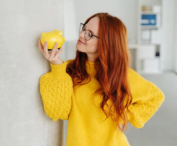 a woman in yellow sweater holding a tiny yellow piggy bank